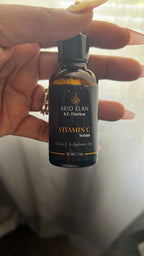 A woman's hand holding a BRIO ÉLAN Vitamin C Serum dropper bottle.